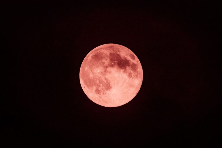 Bulan purnama kemerahan bersinar di langit gelap, ilustrasi Strawberry Moon 2025.
