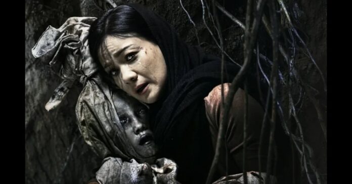 Adegan film Panggilan Dari Kubur—seorang ibu menangis memeluk jasad anaknya di liang gelap berselimut akar.