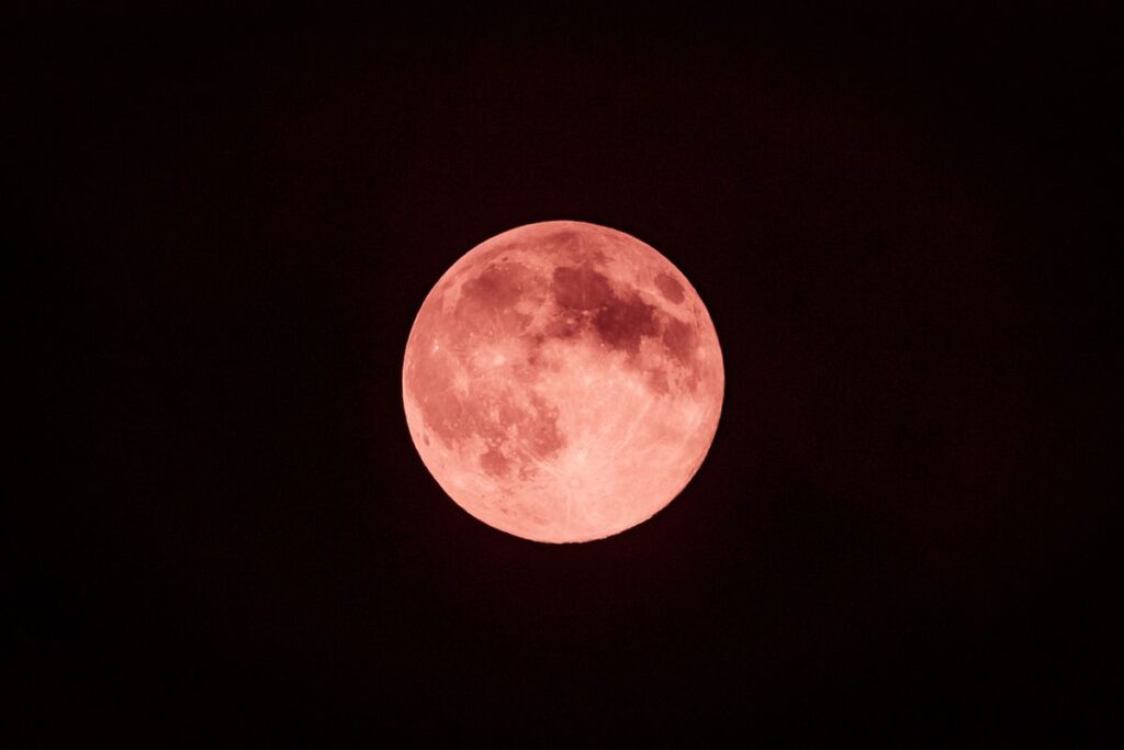 Bulan purnama kemerahan bersinar di langit gelap, ilustrasi Strawberry Moon 2025.