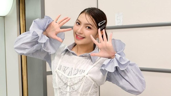 Gracia JKT48 tersenyum cerah sambil berpose tangan membentuk angka sepuluh di belakang panggung.