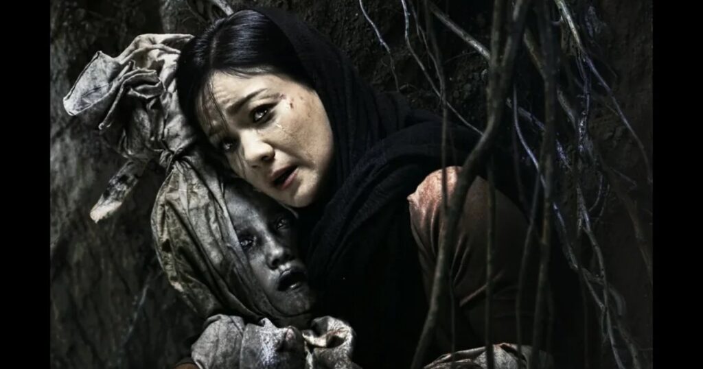 Adegan film Panggilan Dari Kubur—seorang ibu menangis memeluk jasad anaknya di liang gelap berselimut akar.