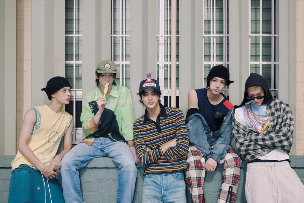 Foto editorial bertema CORTIS—boy group baru HYBE—menampilkan lima remaja bergaya streetwear duduk di depan fasad jendela bernuansa hijau.