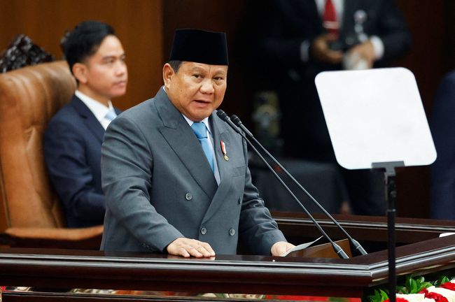 Pidato Kenegaraan: presiden Indonesia berpidato di podium ruang sidang, teleprompter tampak di sisi, suasana parlemen Jakarta.